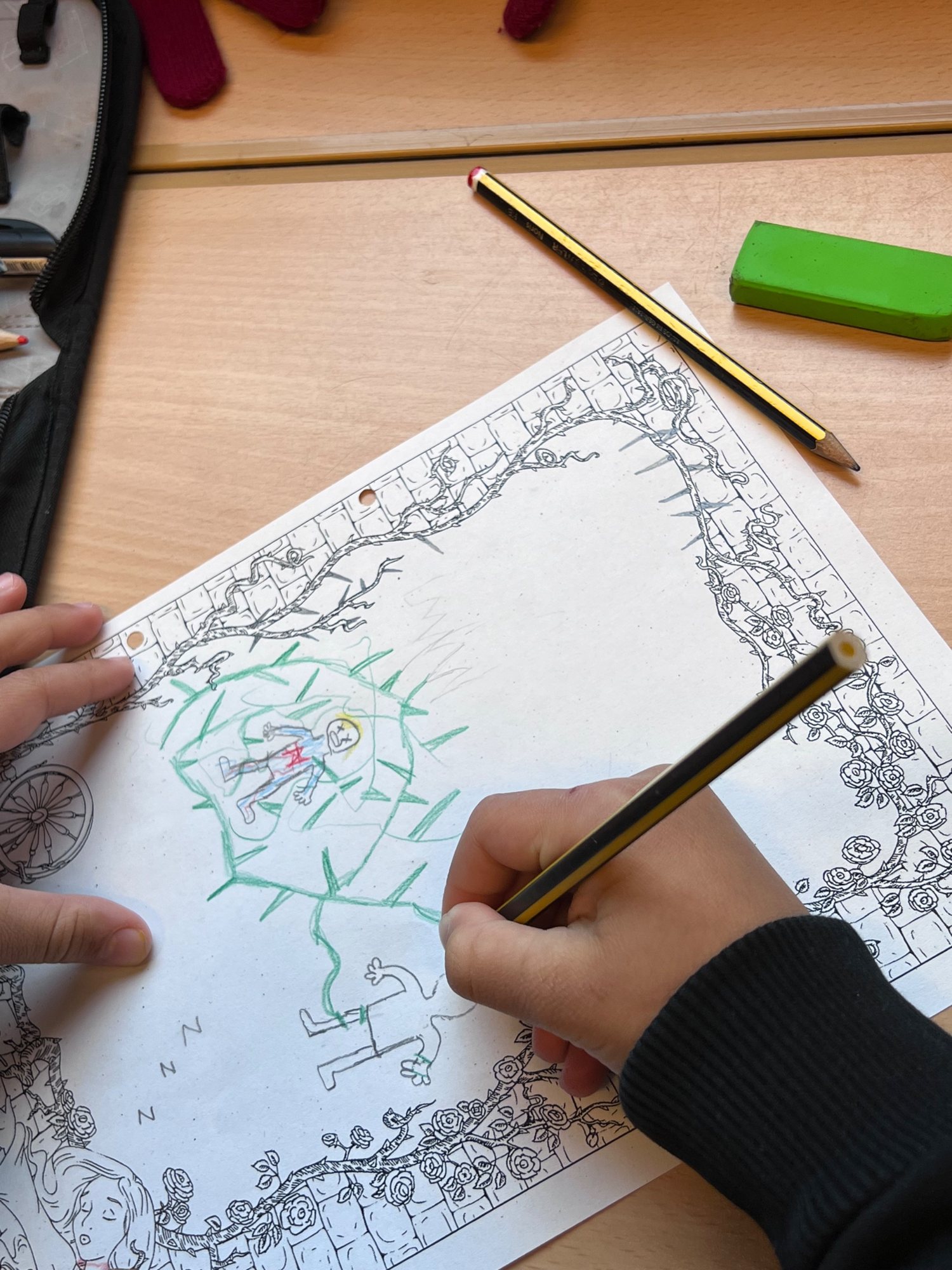 Ein Kind malt mit Buntstiften zum Märchen Dornröschen: der Prinz in der grünen Dornenhecke, umrahmt von Rosenranken