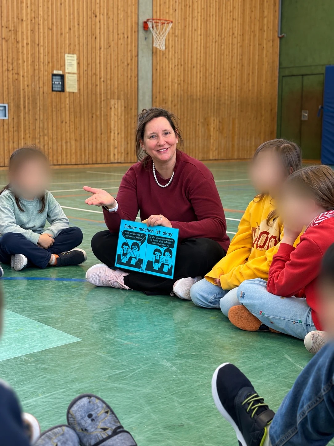 Heike Cordes sitzt mit Kindern im Kreis und zeigt eine Karte mit der Aufschrift „Fehler machen ist okay“